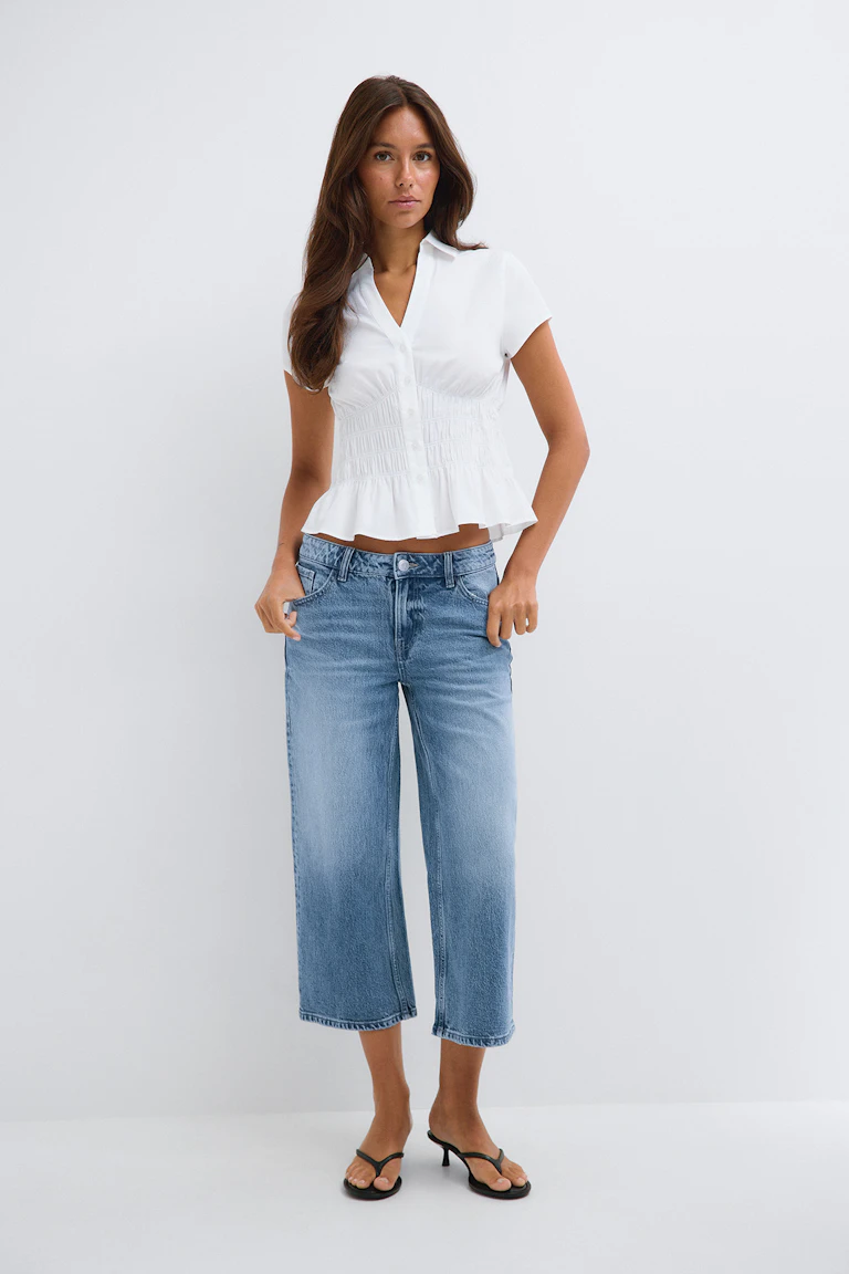 White short-sleeve peplum blouse with a smocked waist, wide-leg cropped blue jeans, and black heeled sandals.