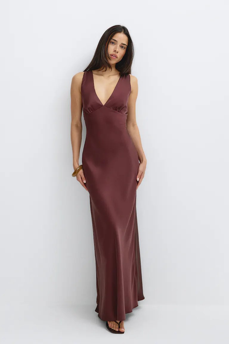 Sleeveless deep‑V floor‑length satin slip dress in burgundy, paired with thin black toe‑strap sandals and a single amber resin bangle.