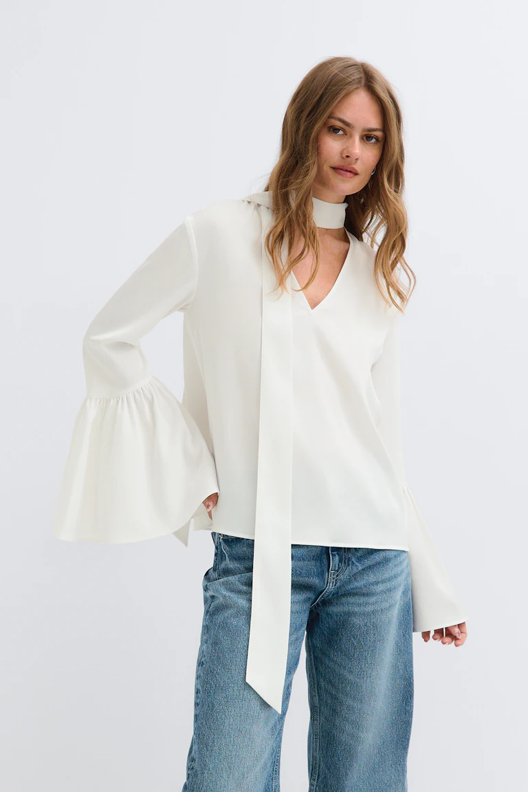 StyleColorSupplier 14423: cremefarbene Bluse mit Bindeband am Hals und ausgestelltem Ärmel sowie blaue Jeans.
