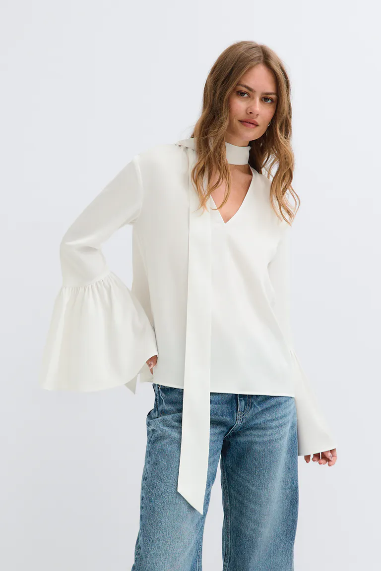 StyleColorSupplier 14423: cremefarbene Bluse mit Bindeband am Hals und ausgestelltem Ärmel sowie blaue Jeans.