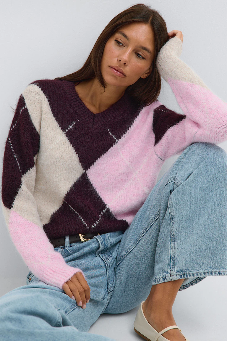 Burgundy, pink, and cream argyle sweater with light-wash jeans and cream flats.