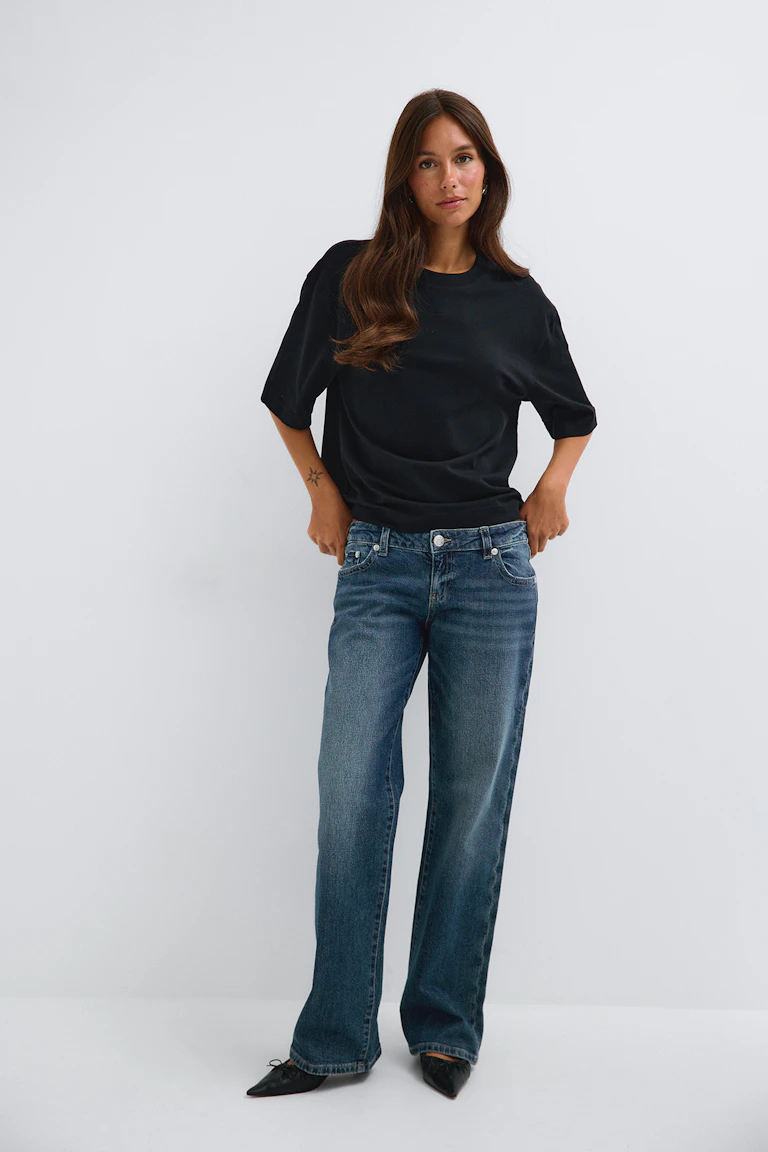 Black short-sleeve top with blue straight-leg jeans and black pointed flats.