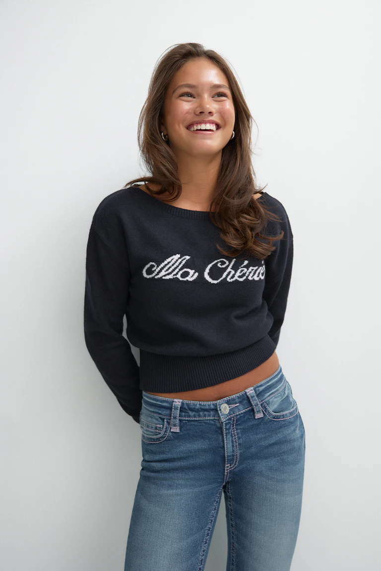Pull noir en maille à logo, porté avec un jean bleu.