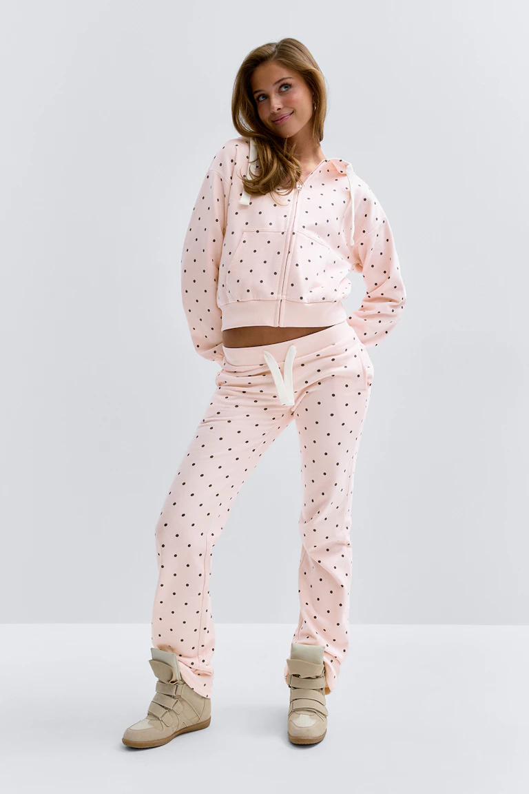 Ljusrosa croppad hoodie med dragkedja och mönster av små svarta prickar, matchad med matchande sweatpants med dragsko och beige high-top wedge sneakers.