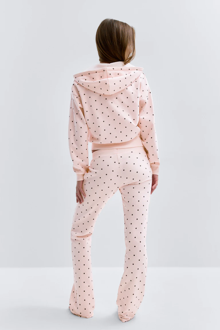 Ljusrosa sweatshirt med huva och matchande utsvängda byxor med hög midja, båda tryckta med små svarta prickar.