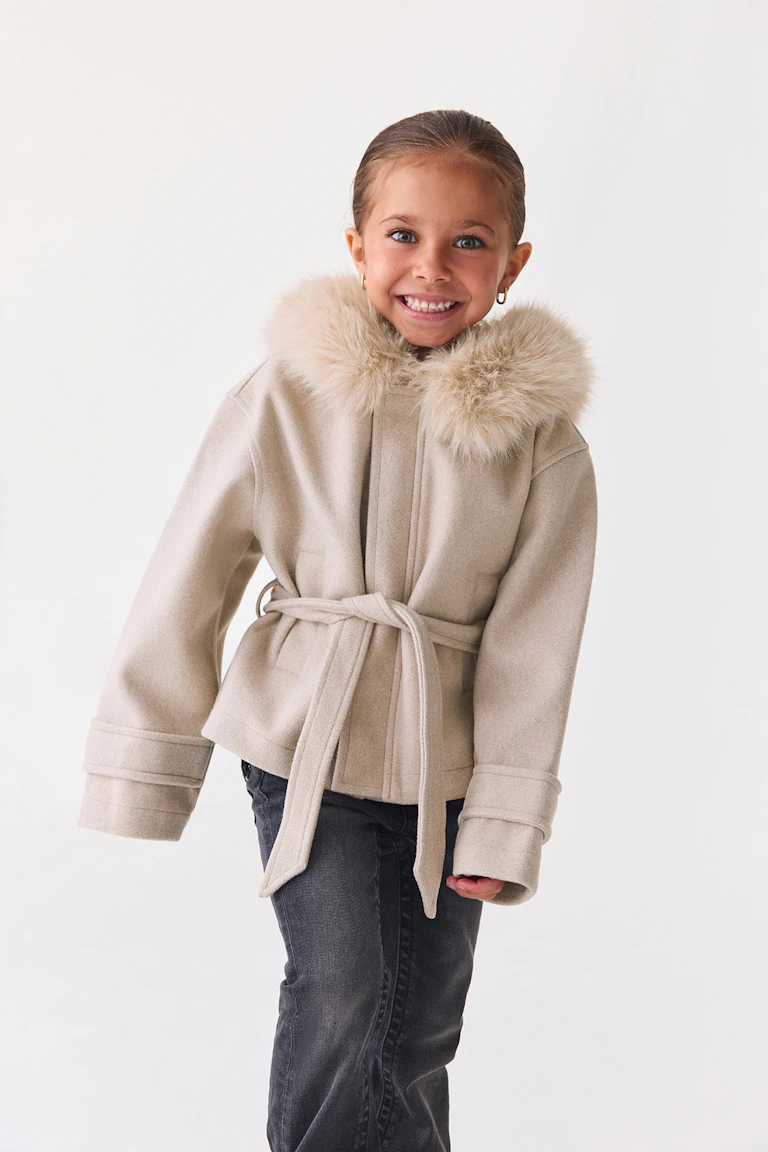 Id 324256, StyleColorSupplier 14651: Beige frakke med bælte og kant af imiteret pels, kombineret med mørke jeans.
