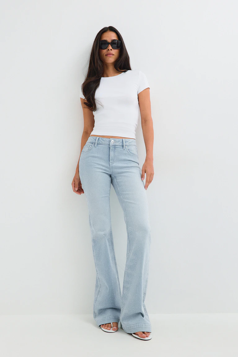 White fitted short-sleeve top, light blue embellished flared jeans, black sunglasses, and white sandals.