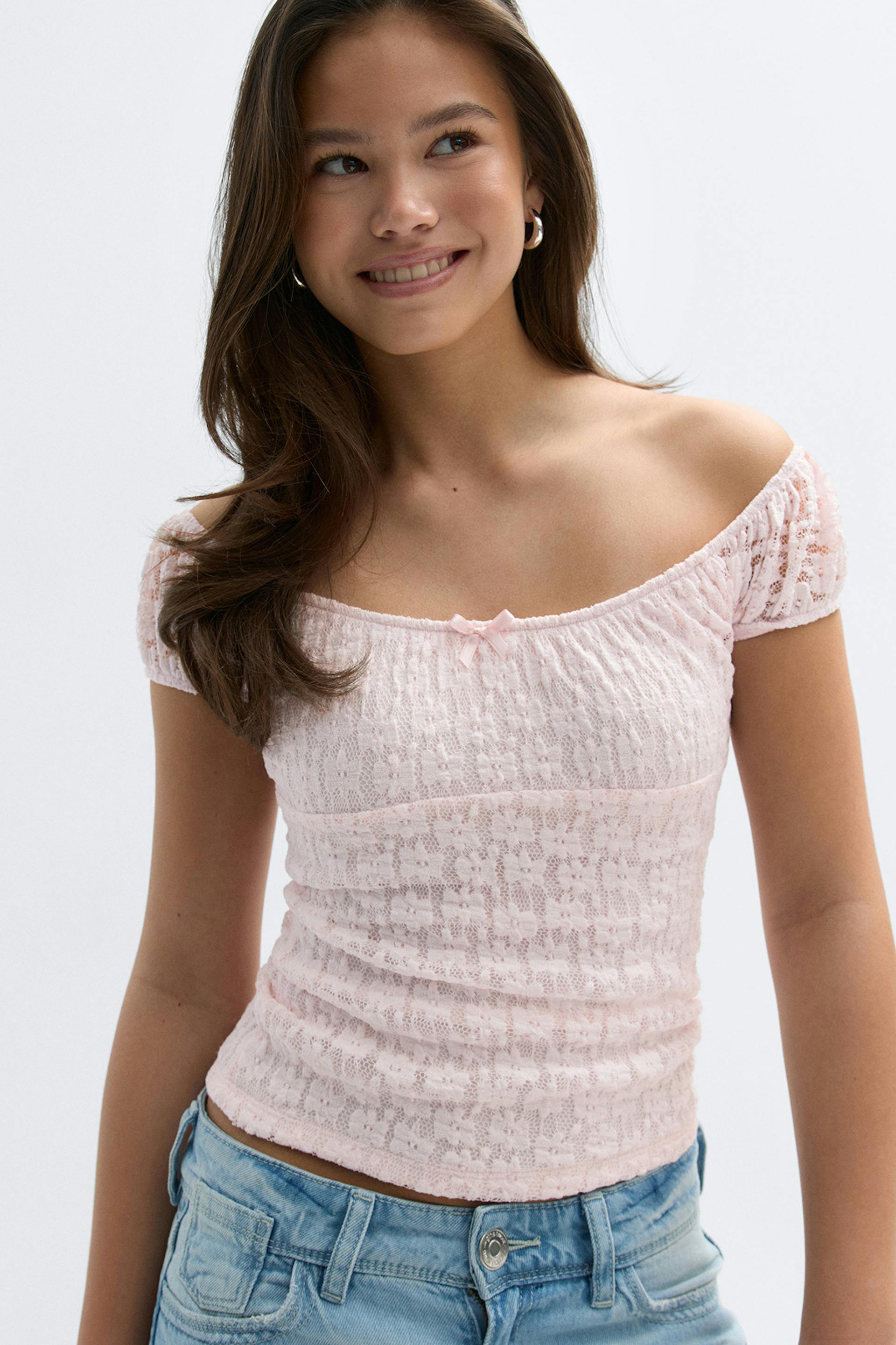 Top à manches courtes en dentelle rose pâle avec un petit nœud sur le devant, associé à un jean taille basse délavé.