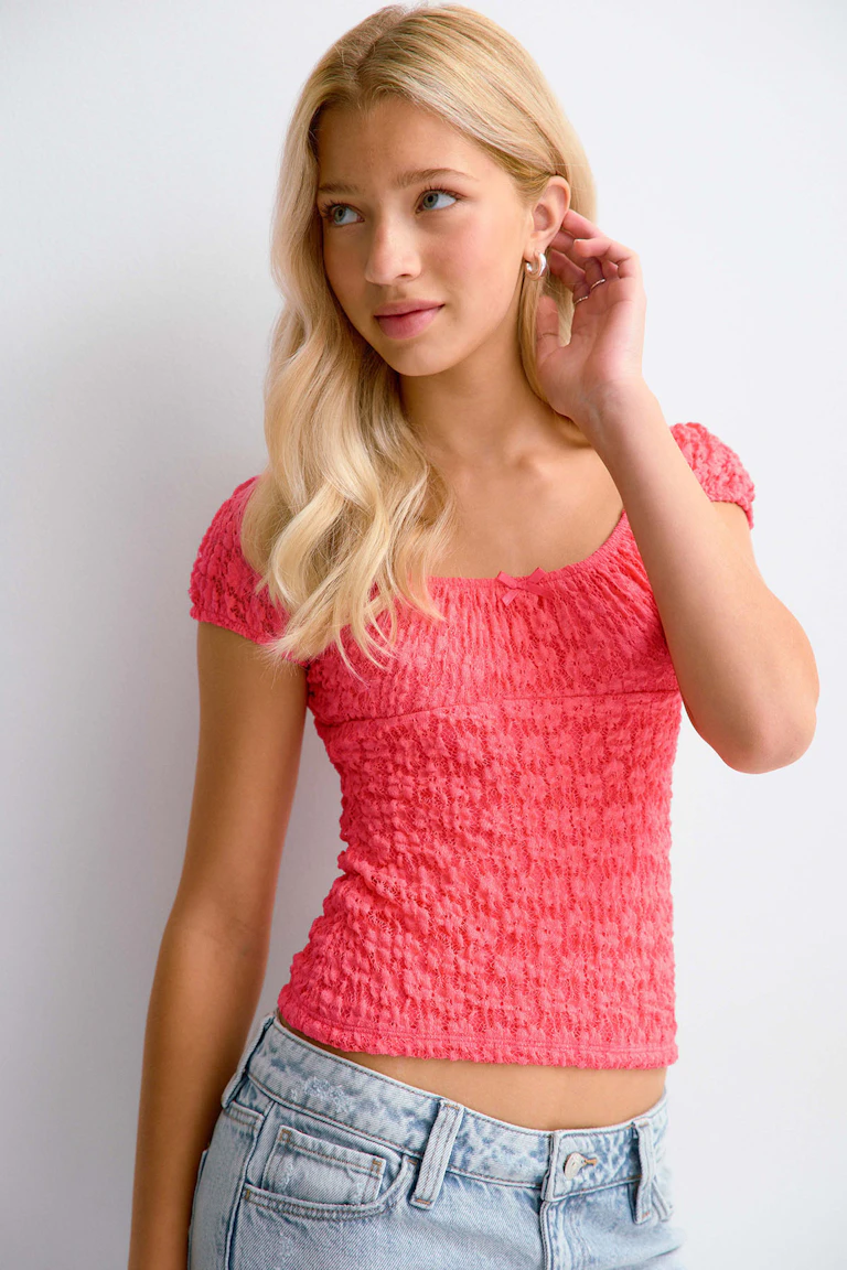 Coral smocked short-sleeve top with scoop neckline paired with white distressed denim shorts with frayed hems.