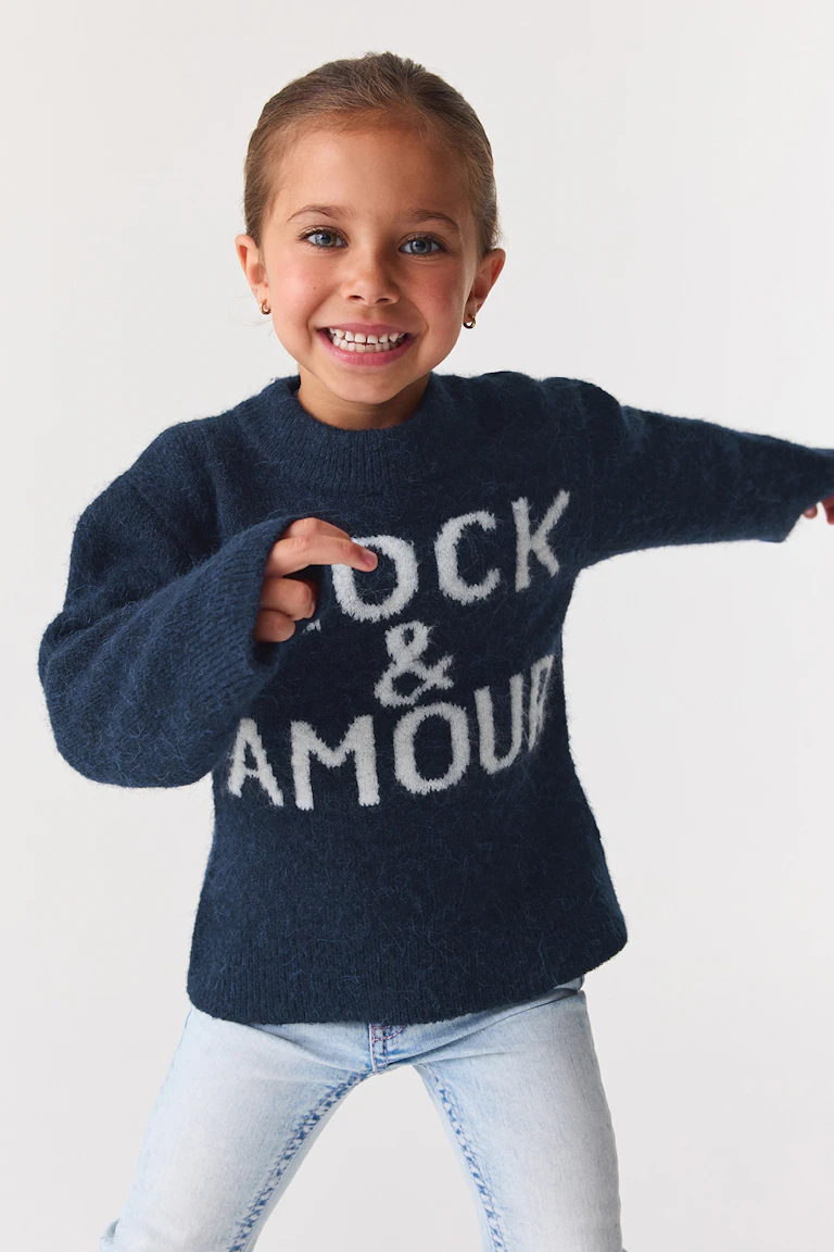 Dark navy fuzzy sweater with white lettering, paired with light-wash jeans.