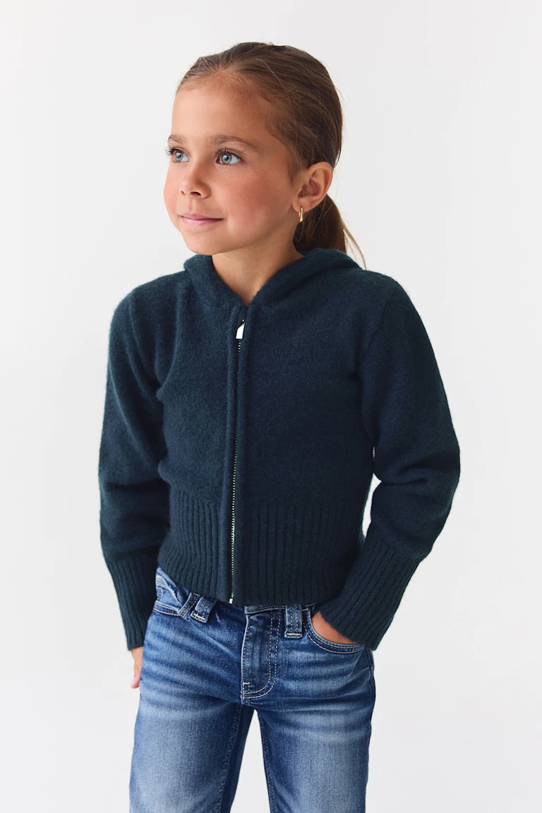 Dunkelblaue Strickjacke mit Reißverschluss vorne, gerippten Bündchen und blauen Jeans.