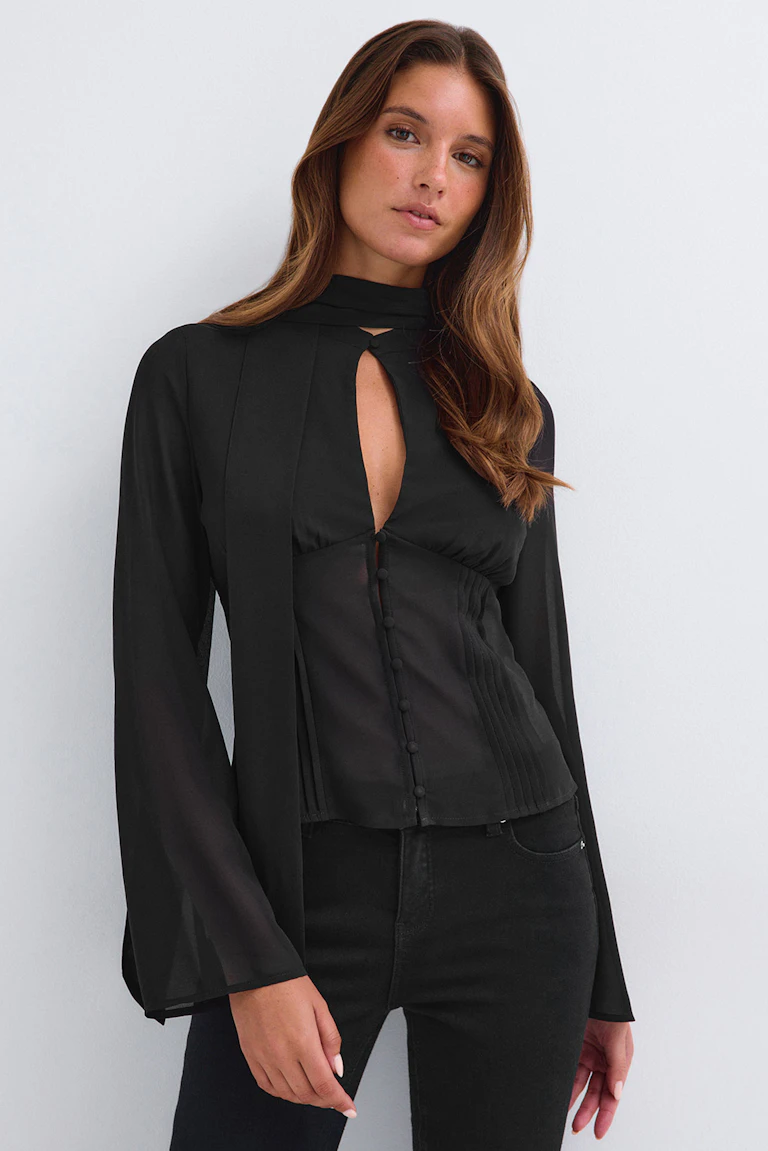 Id 331773, StyleColorSupplier 14423: Sort, gennemsigtig langærmet bluse med høj hals og nøglehulsudskæring, kombineret med sorte bukser.
