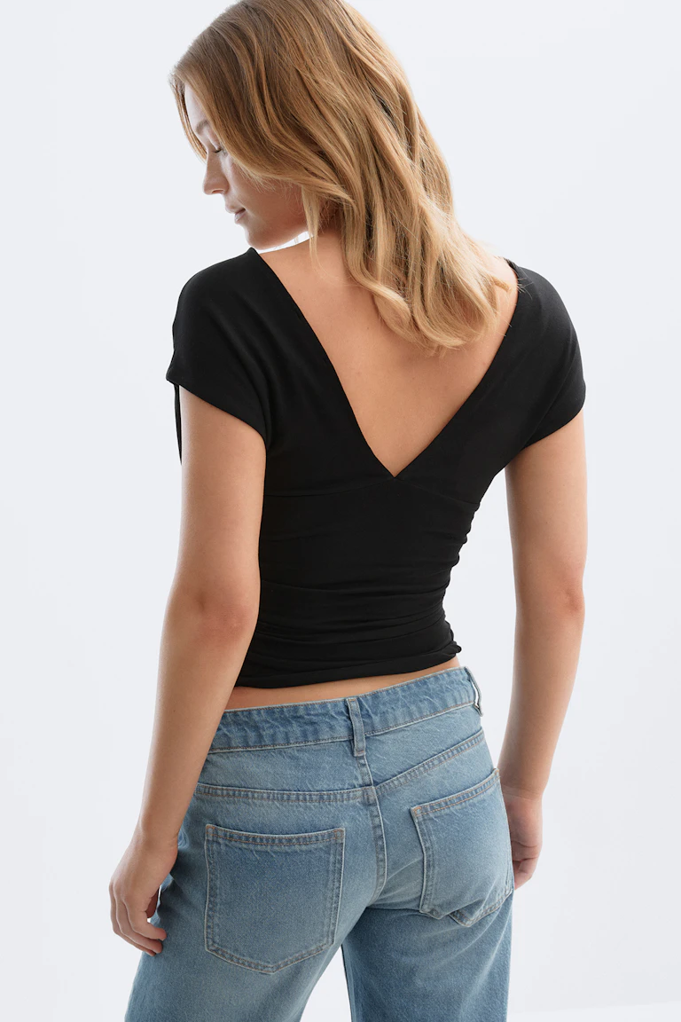 Schwarzes, kurzärmeliges, tailliertes Oberteil mit tiefem V-Ausschnitt, kombiniert mit hellen Jeans mit geradem Bein und aufgesetzten Taschen hinten.