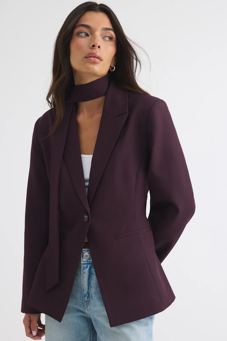 Dark plum blazer with a matching neck scarf, worn over a white top and light blue jeans.