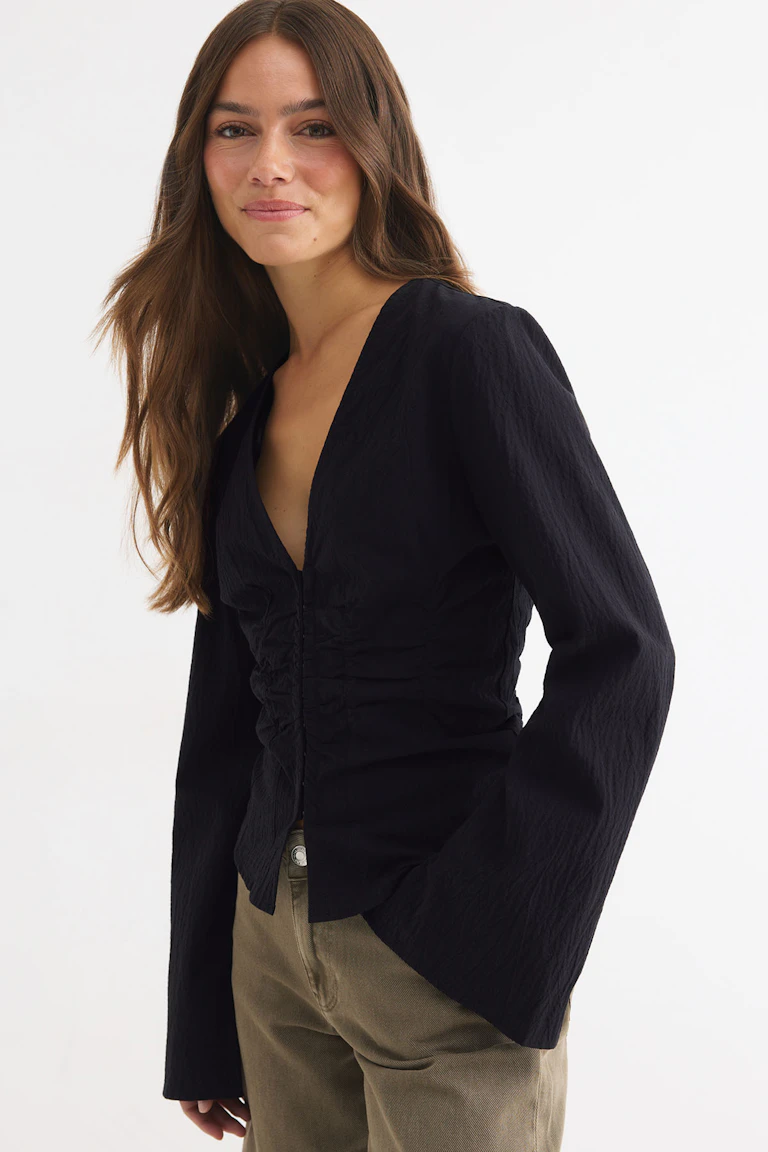 ID 330510 | StyleColorSupplier 14423: Schwarze Langarmbluse mit V-Ausschnitt, geraffter Vorderseite und beiger Hose.