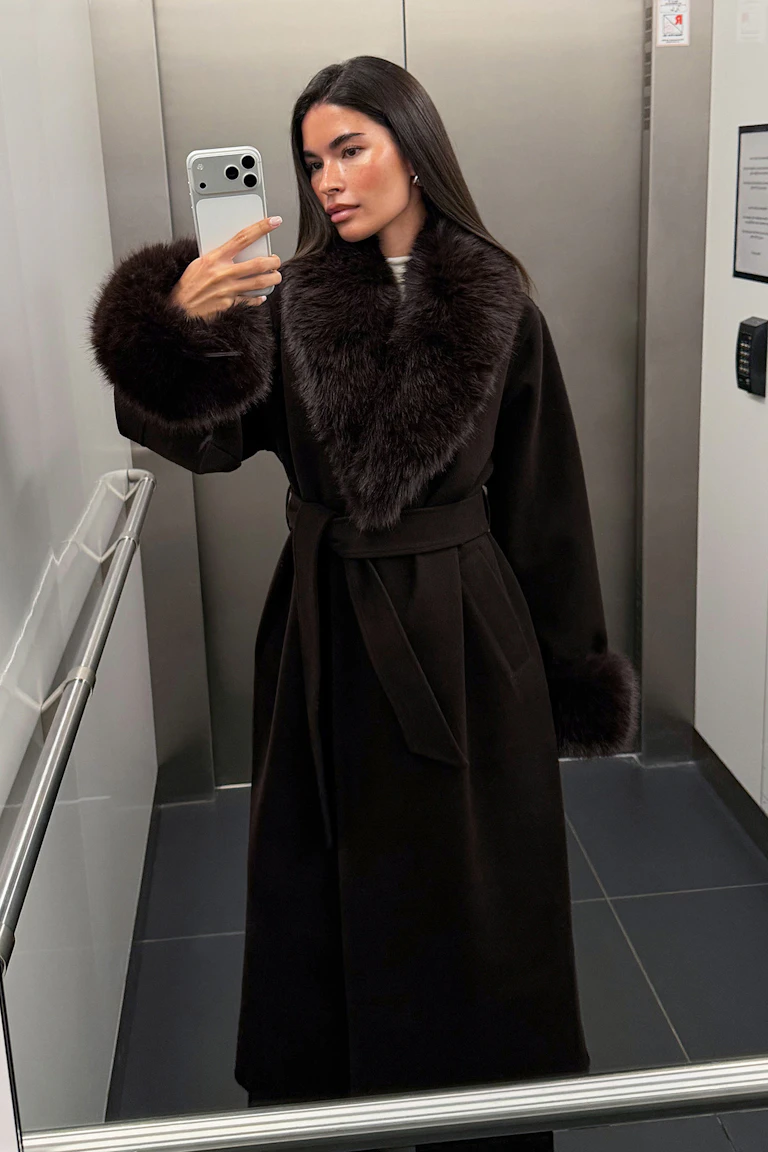 Long dark belted coat with oversized fur collar and matching fur cuffs.