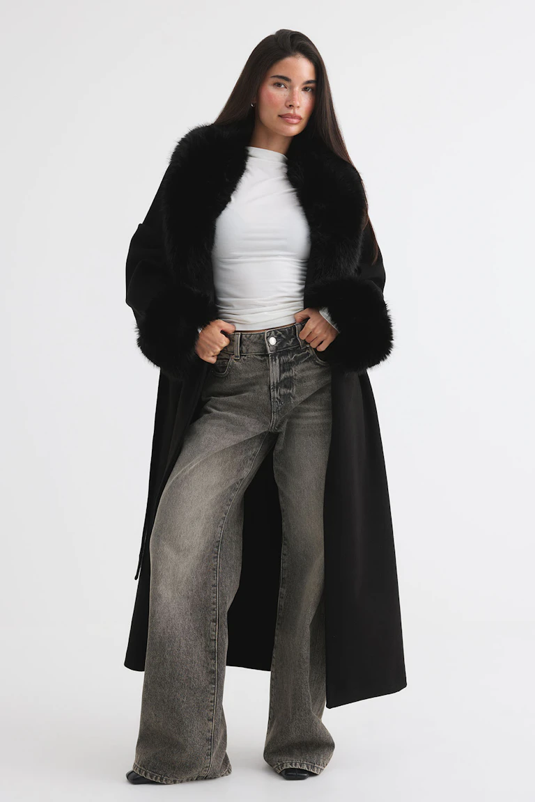 Black coat with faux fur trim, white fitted top, and grey wide-leg jeans.