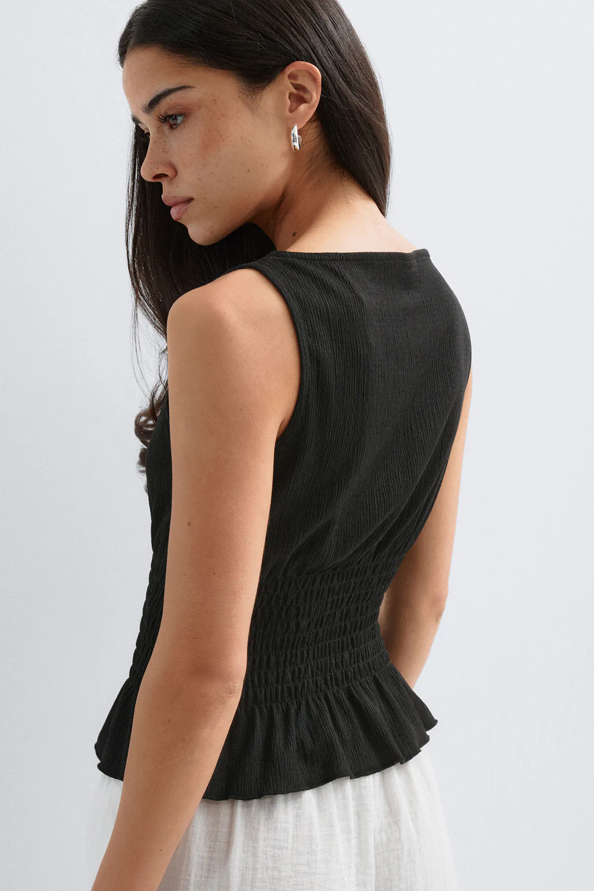 Hihaton musta kuvioitu yläosa, jossa on smokattu vyötärö ja peplum-helma, yhdistettynä valkoiseen hameeseen ja hopeisiin korvakoruihin.