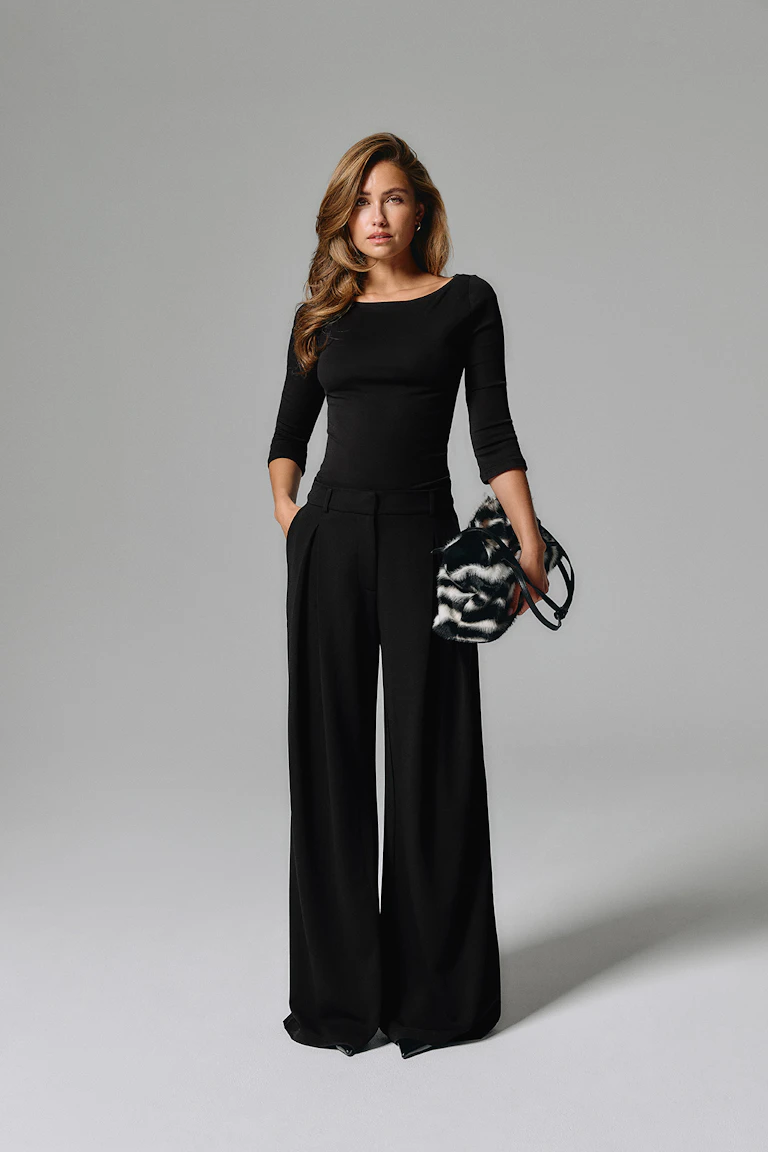 Black fitted three-quarter-sleeve top with wide-leg black trousers and a black-and-white patterned handbag.