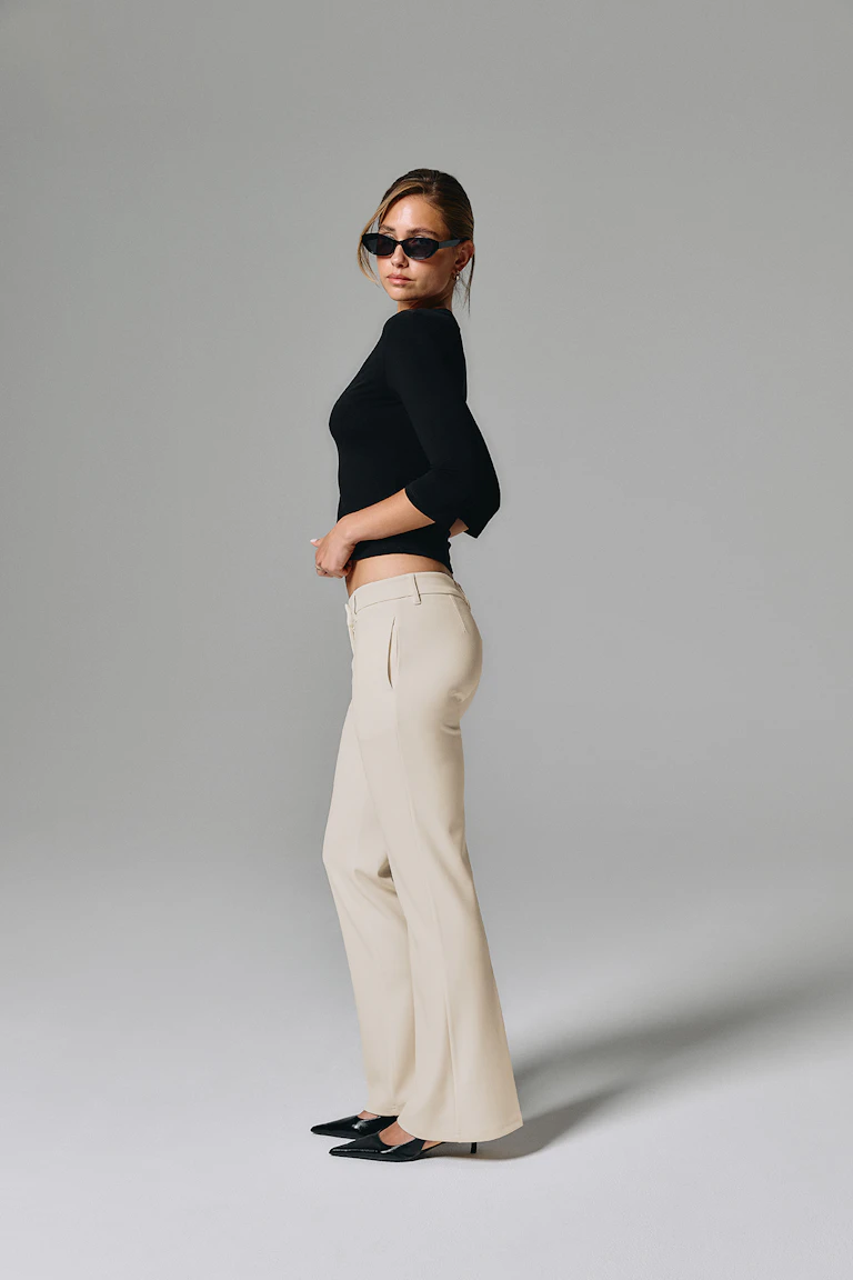 Black fitted top with cream wide-leg trousers, black pointed heels, and black sunglasses.