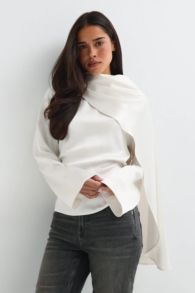 ID 327935: Witte, gedrapeerde top met lange mouwen en een cape-achtige overlay, gecombineerd met een donkere jeans met rechte pijpen. StyleColorSupplier 14423.