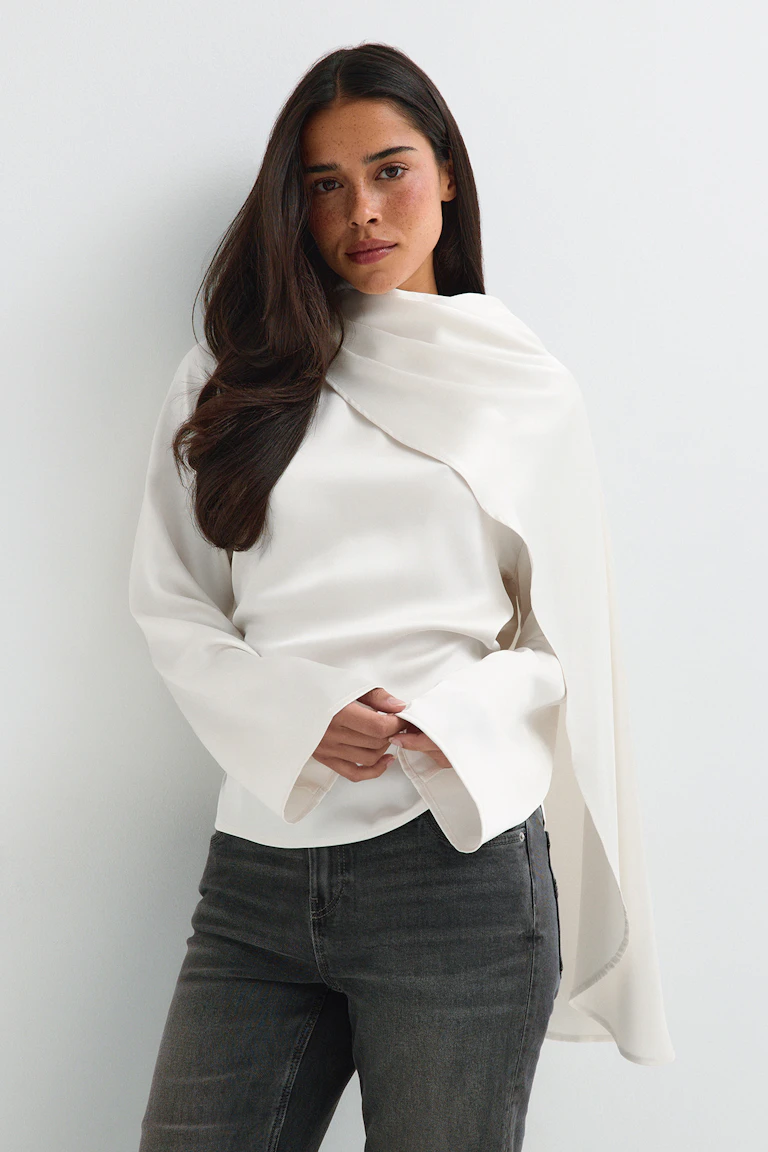 ID 327935: Witte, gedrapeerde top met lange mouwen en een cape-achtige overlay, gecombineerd met een donkere jeans met rechte pijpen. StyleColorSupplier 14423.