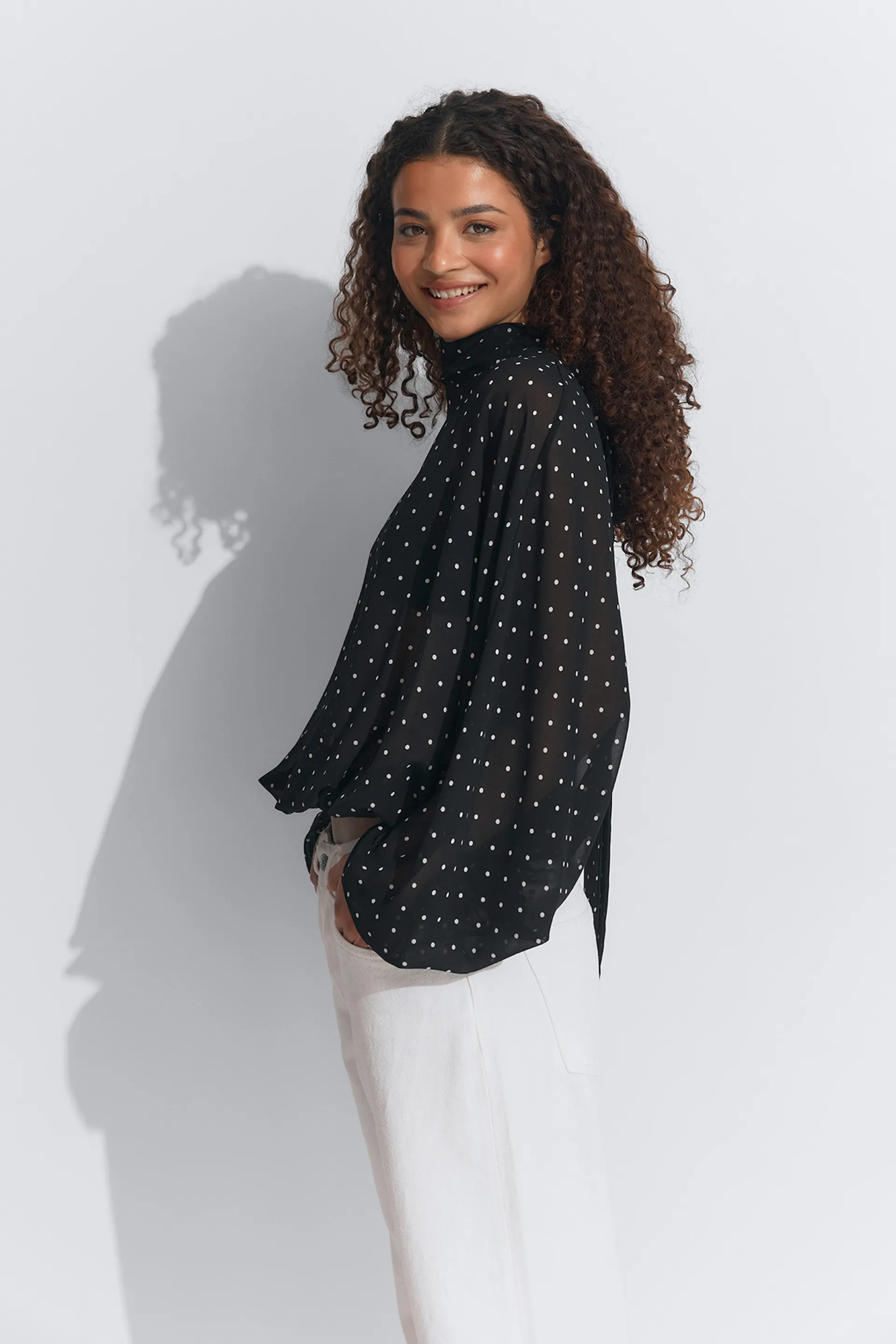 Svart skir prickig blus med hög halsringning och böljande långa ärmar, kombinerad med vita byxor med hög midja.