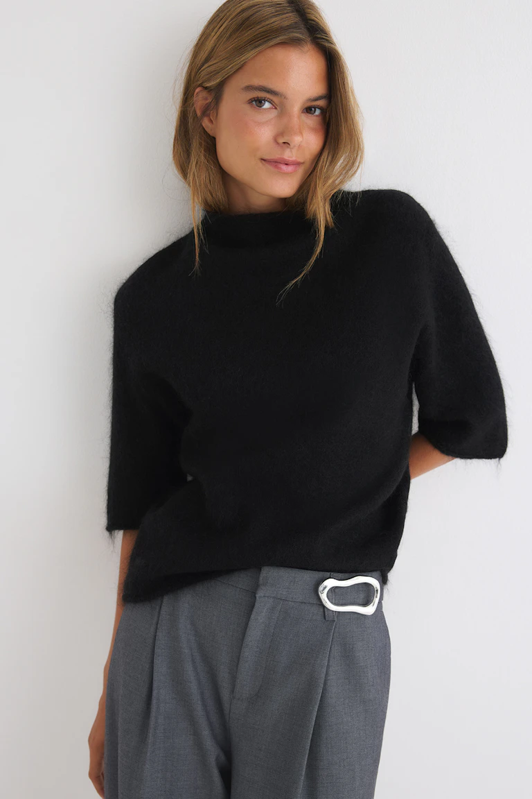 Schwarzer, flauschiger Kurzarmpullover mit grauer, taillierter Hose und einem Gürtel mit silberner Schnalle.