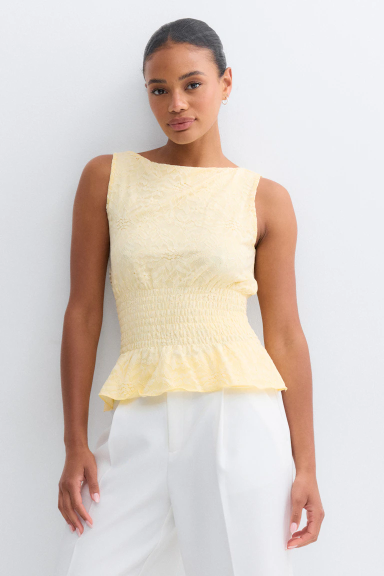 Top en dentelle jaune pâle sans manches avec encolure bateau, taille smockée froncée et ourlet péplum, associé à un pantalon blanc taille haute.