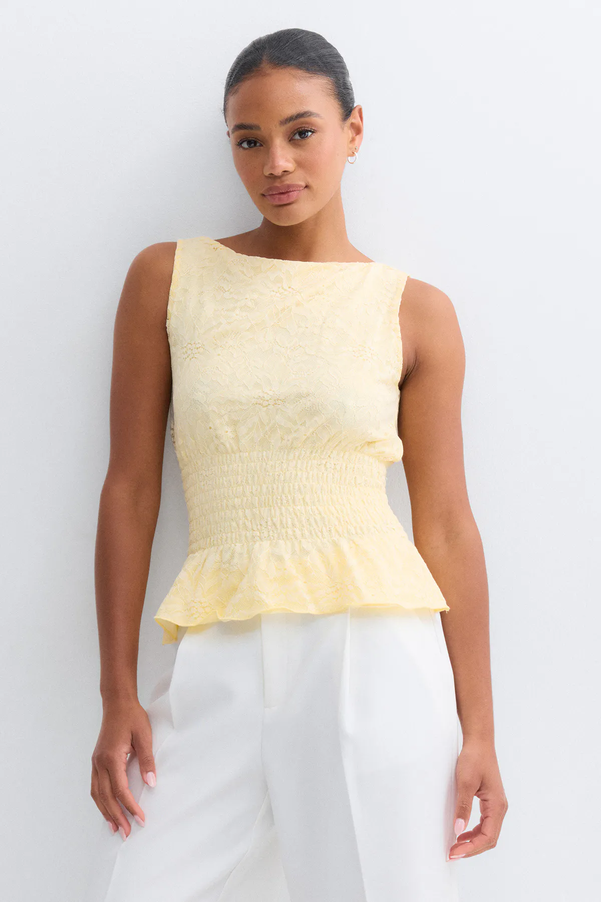 Top en dentelle jaune pâle sans manches avec encolure bateau, taille smockée froncée et ourlet péplum, associé à un pantalon blanc taille haute.