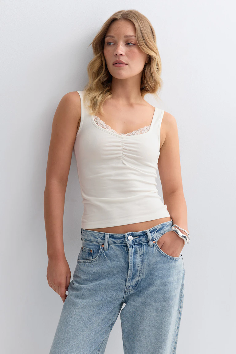 Ivoorkleurige tank met kanten randje en subtiele ruches aan de voorkant, gecombineerd met een lichtgekleurde, relaxte jeans en een zilveren manchet-armband.