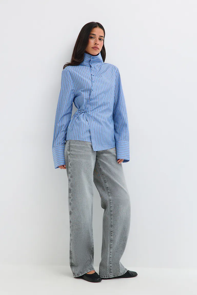 Ein blau gestreiftes Shirt mit hohem Kragen, dazu eine graue Jeans mit weitem Bein und schwarze Ballerinas.