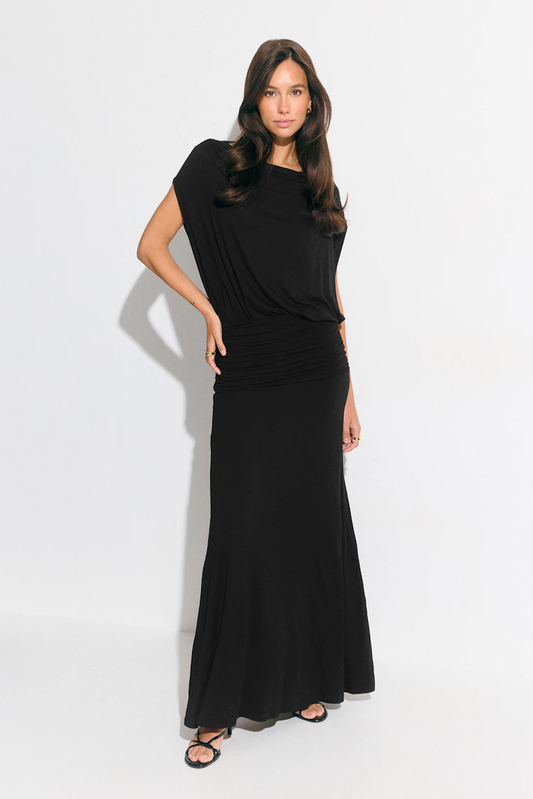 Black draped short-sleeve maxi dress with a ruched waistband, paired with black strappy sandals and gold hoop earring and rings.