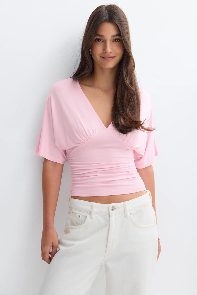 Lichtroze top met V-hals en ruches en wijde korte (fladder)mouwen, gecombineerd met een ivoorkleurige jeans met hoge taille.