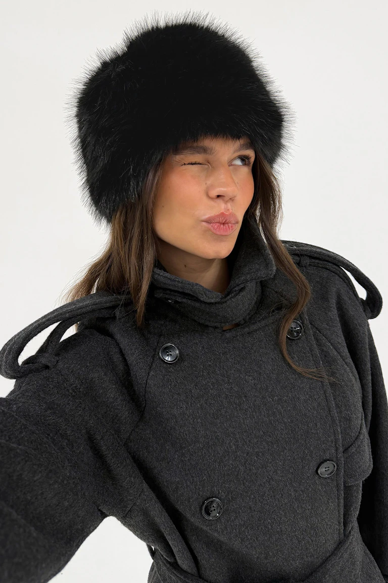 The person wears a black fur hat and a charcoal double-breasted coat.