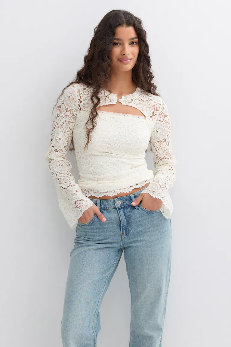 Elfenbensfarvet, langærmet bolero i blomstret blonde med skulpterede kanter over en matchende stropløs blonde-camisole, sat sammen med lysvaskede jeans med lige ben.