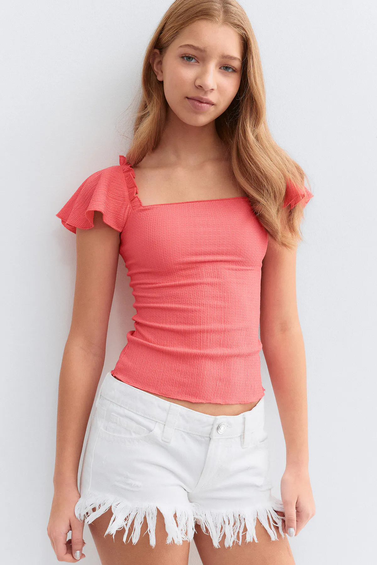 Top à col carré ajusté en côtes corail et manches courtes à volants, associé à un short en denim blanc à ourlet effiloché.