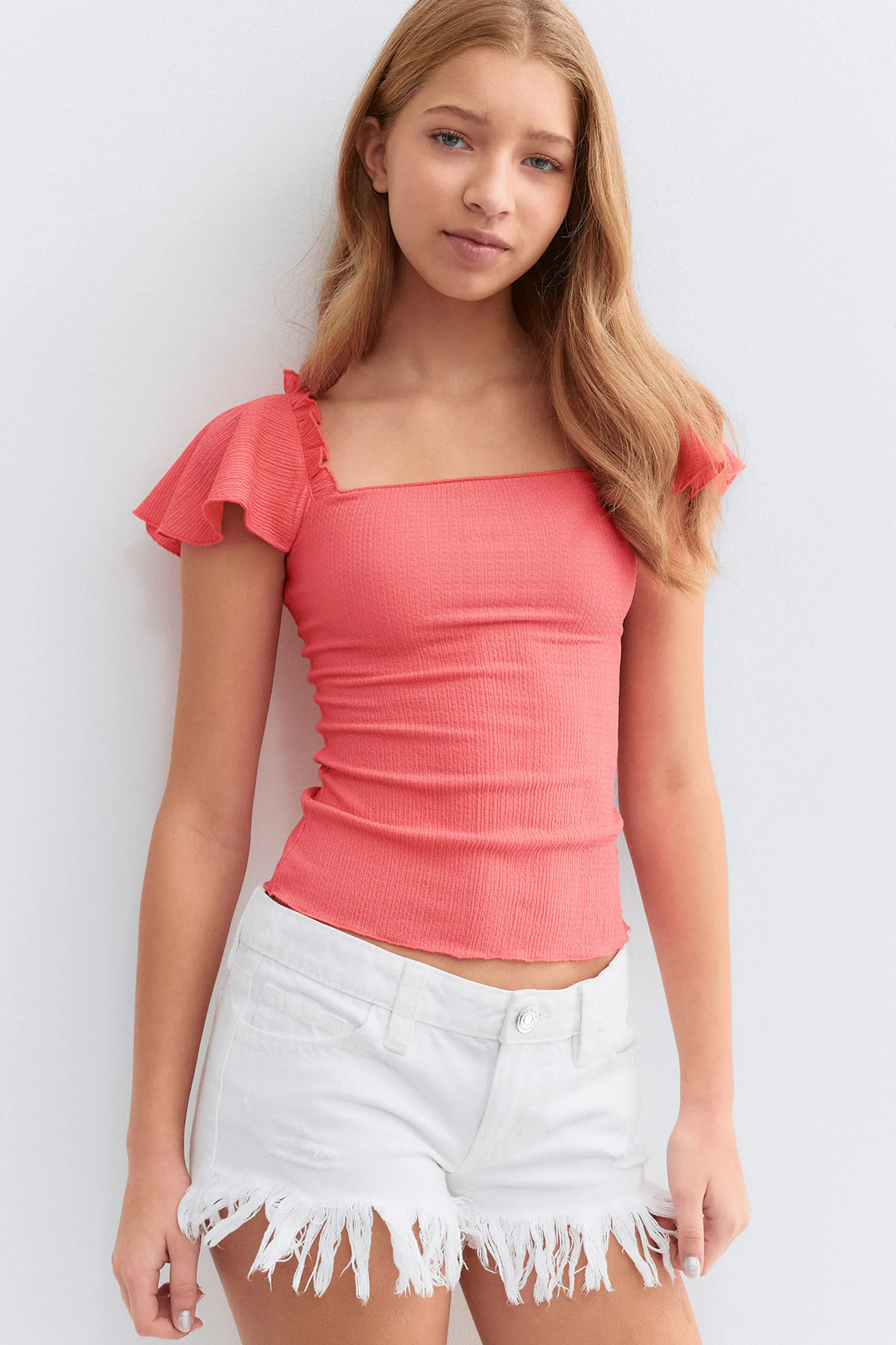 Top à col carré ajusté en côtes corail et manches courtes à volants, associé à un short en denim blanc à ourlet effiloché.