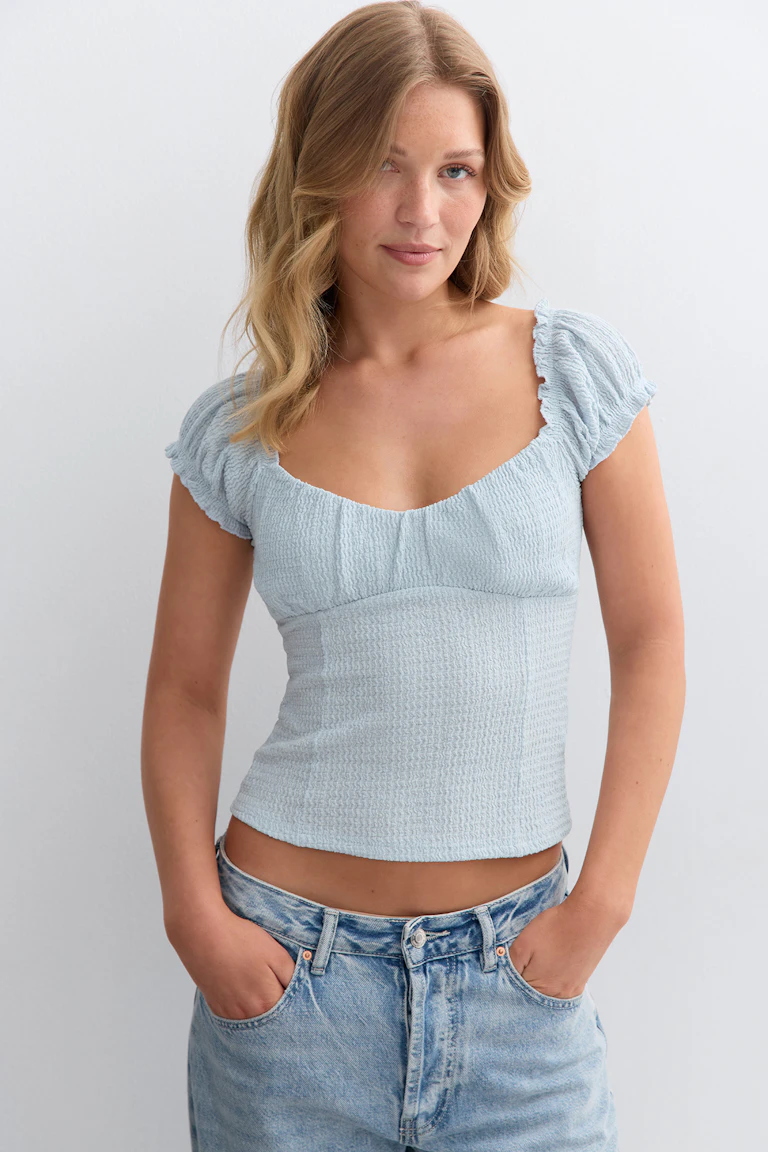 Lichtblauwe gesmokte top met korte mouwen en ruches, pofmouwen en een vierkante hals, gecombineerd met een faded light-wash denim jeans.