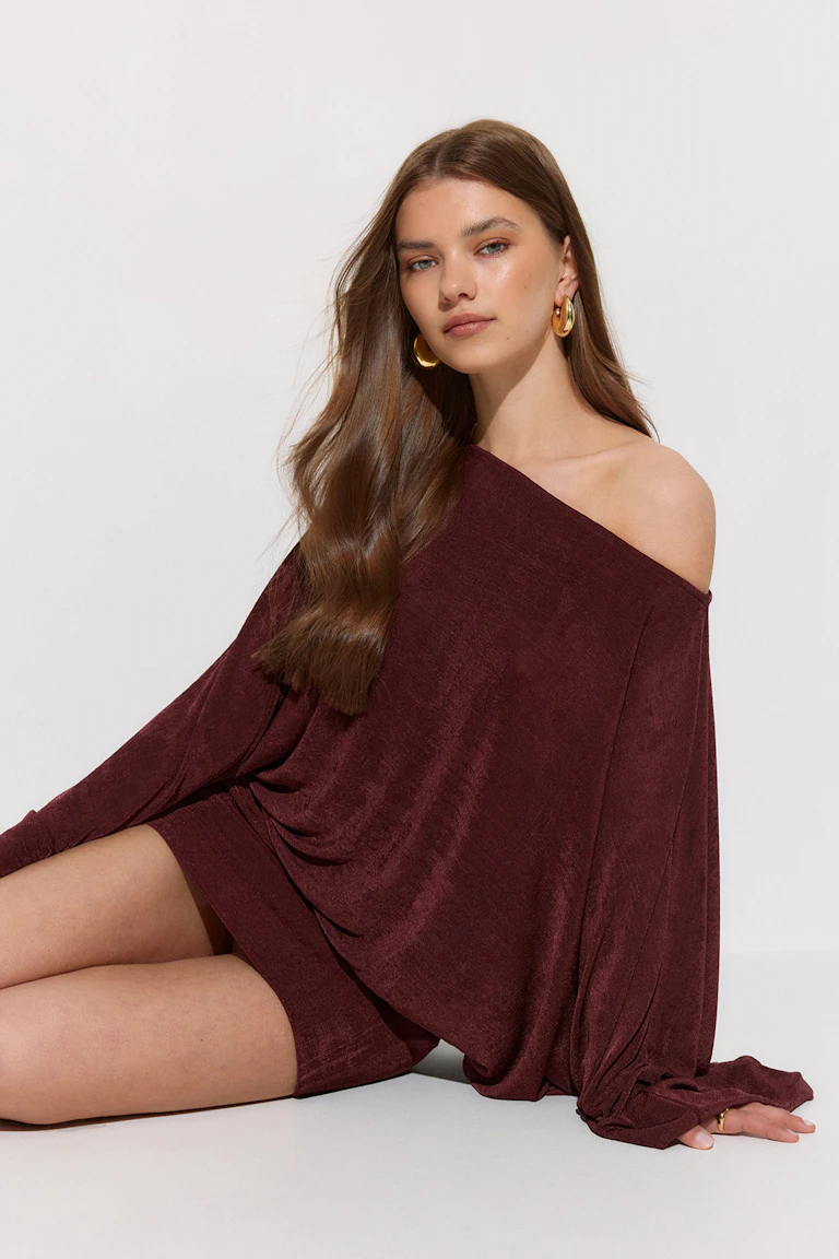 Off-the-shoulder dyb bordeaux fløjlsdraperet minikjole med rynkede ballonærmer, stylet med store guldøreringe og en guldring.