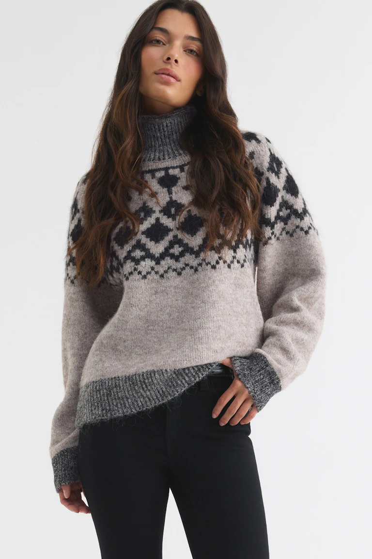Beige and black patterned turtleneck sweater with ribbed cuffs, paired with black trousers.