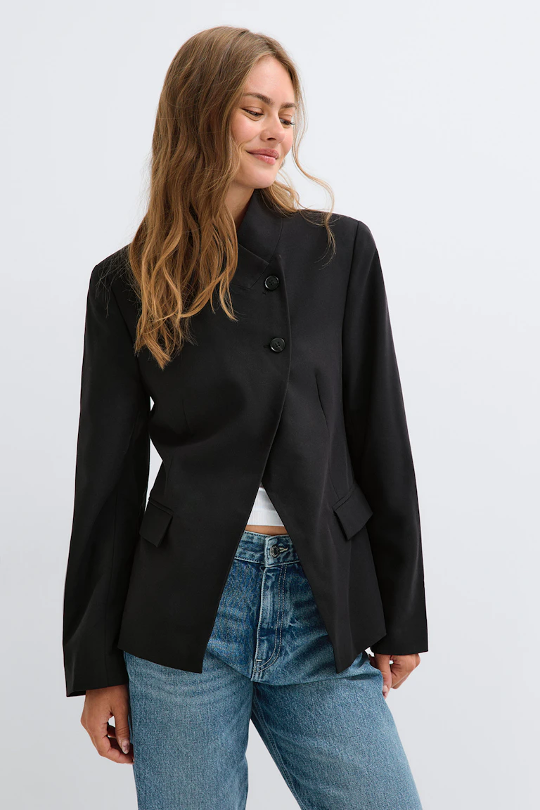 Een zwarte, getailleerde blazer over een witte cropped top en een blauwe spijkerbroek.