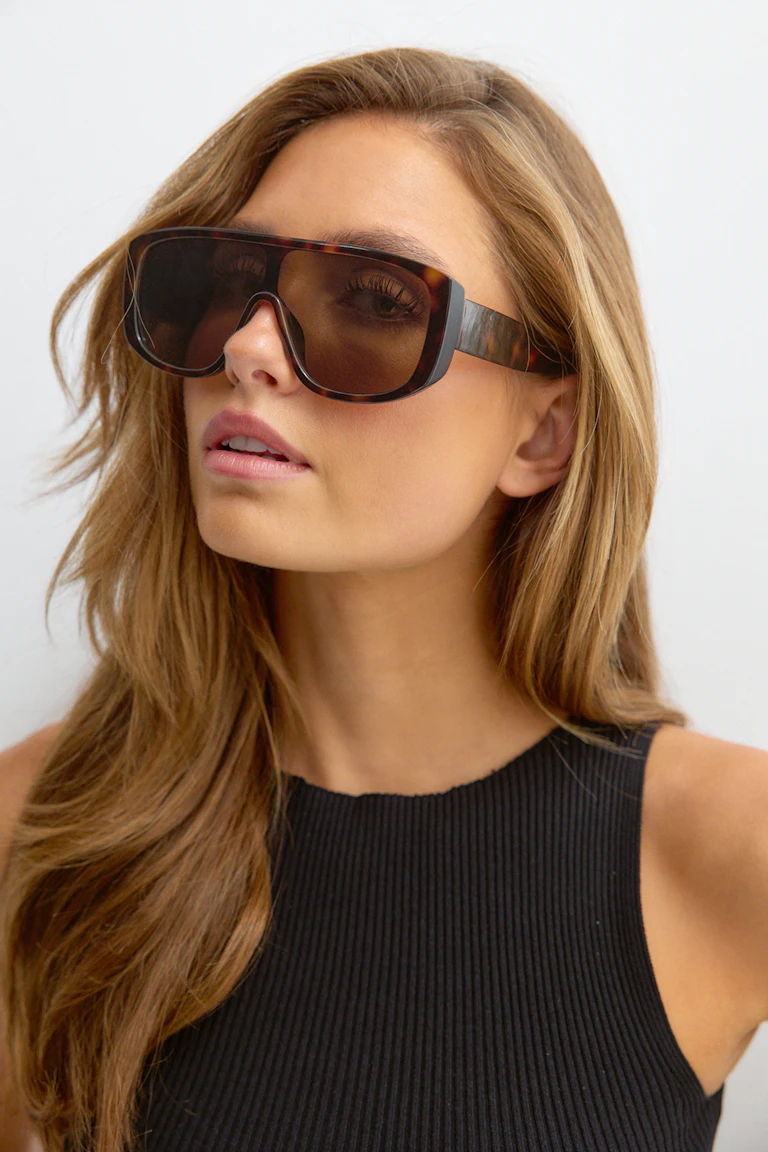 Woman wearing large tortoiseshell shield sunglasses and a black ribbed sleeveless top.