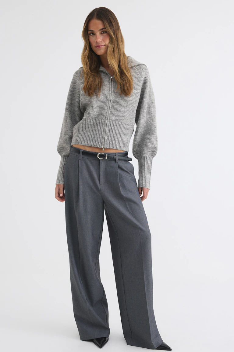 ID 334237 | StyleColorSupplier 12006: Grauer, gerippter Strickpullover mit Reißverschluss vorne, dazu eine weit geschnittene, anthrazitfarbene Hose, ein passender Gürtel und schwarze spitze Schuhe.