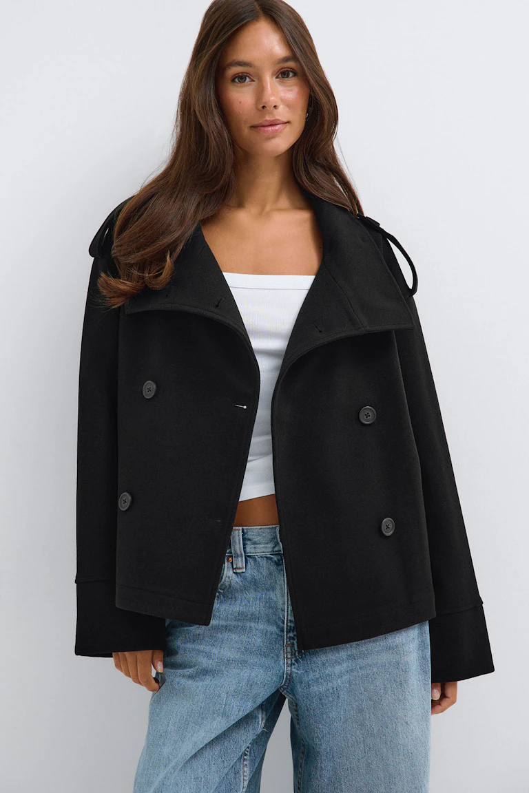 Une veste noire à double boutonnage portée par-dessus un haut blanc et un jean bleu clair.