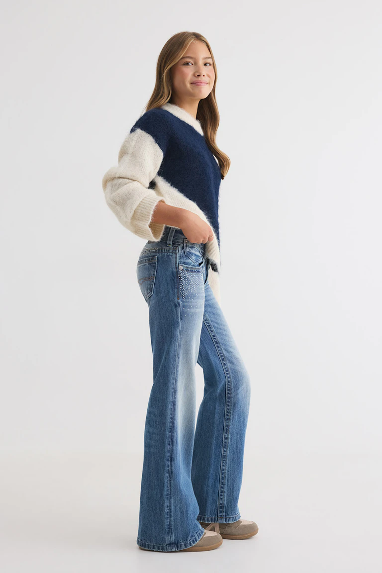 Ein cremefarbener und marineblauer Pullover im Color-Blocking-Look, dazu eine blaue Jeans mit weitem Bein und Verzierungen sowie beigefarbene Sneaker.