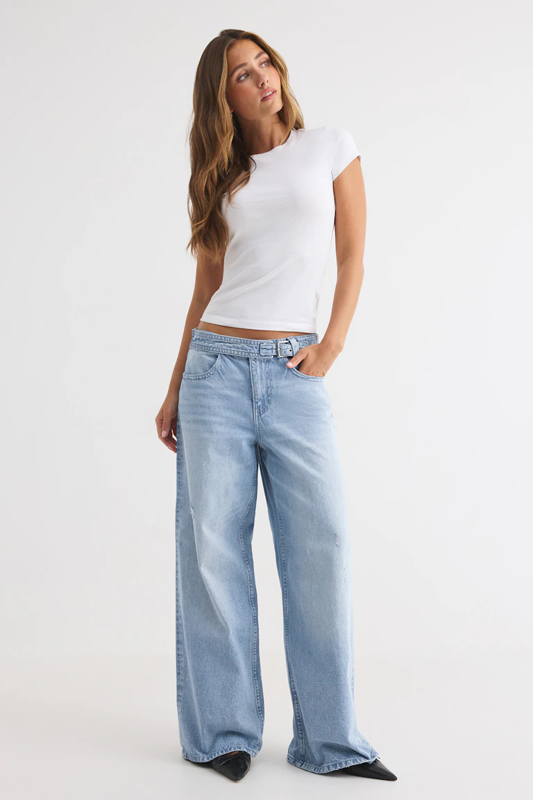id 332273, StyleColorSupplier 17919: Wit, nauwsluitend T-shirt met korte mouwen, lichtgekleurde jeans met wijde pijpen en zwarte schoenen met spitse neus.