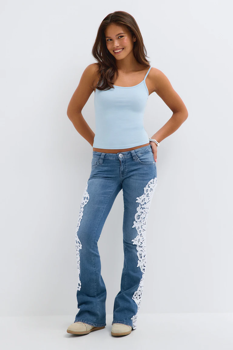 Lyseblå camisole med blå jeans, hvide blondepaneler i siderne og beige flade sko.