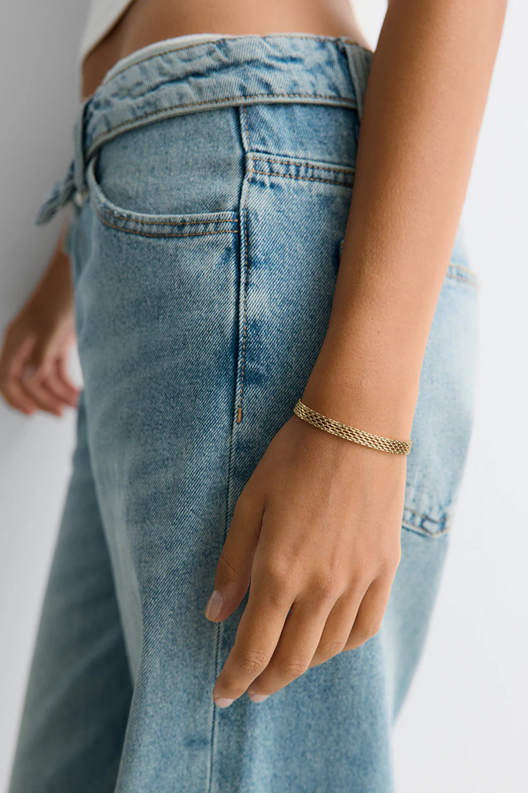 Model in hellblauen Jeans und einem geflochtenen goldenen Armband. StyleColorSupplier: 16819.