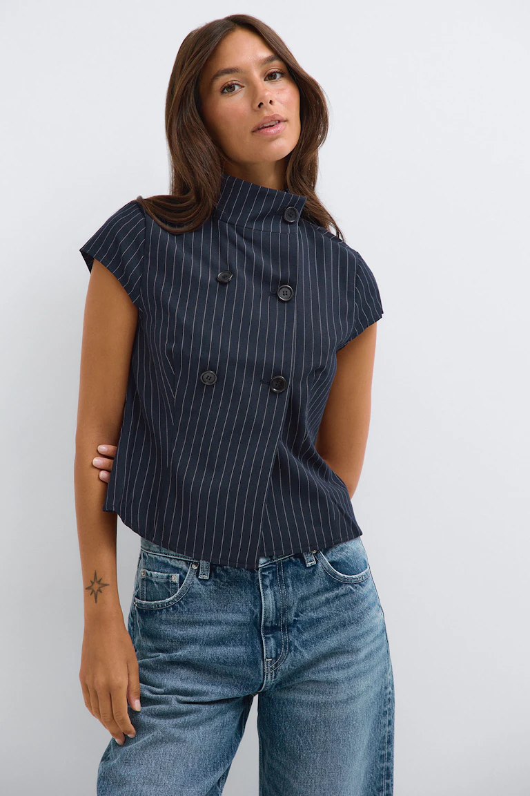 Référence 332719, StyleColorSupplier 16657 : haut sans manches à double boutonnage à fines rayures bleu marine, porté avec un jean bleu.